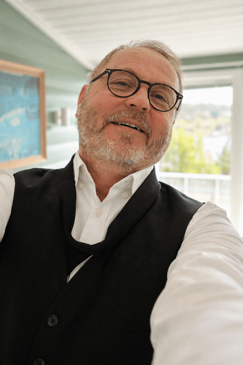 Birger sitter ute pÄ terrasse ved hytta med caps og solbriller.