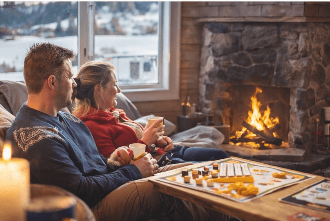 To personer med varm drikke foran peisen pÄ hytta